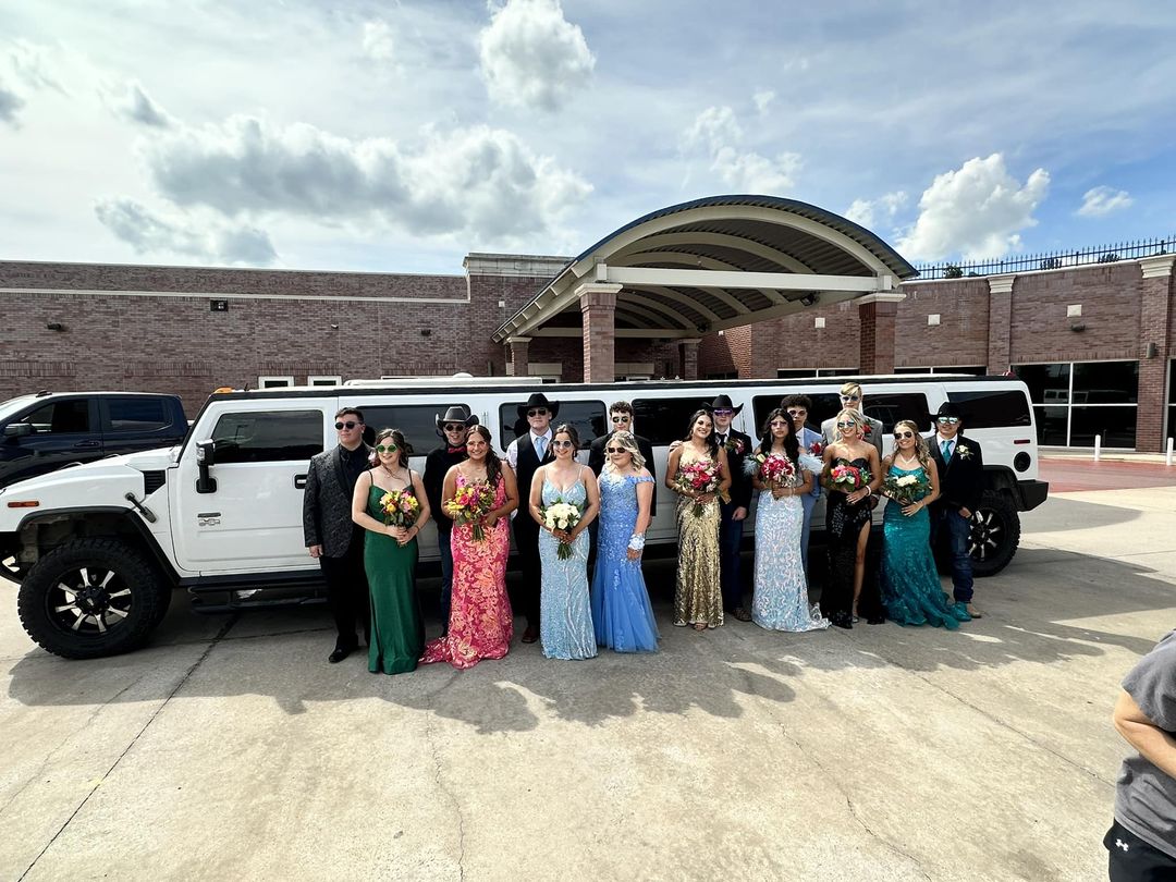 Prom goers pose by white limousine.