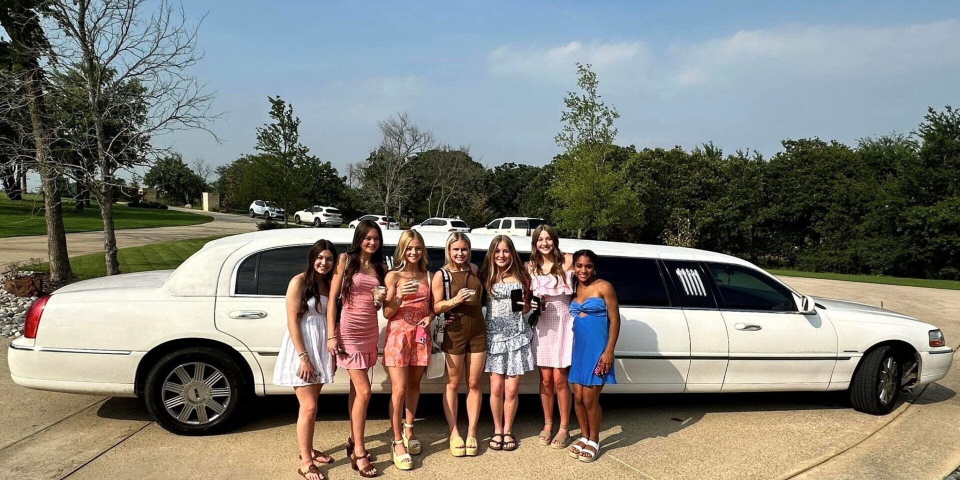 Seven girls pose by a white limo.